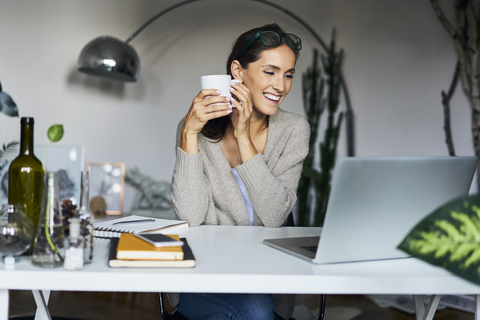 Happy young woman at home with laptop on desk stock photo