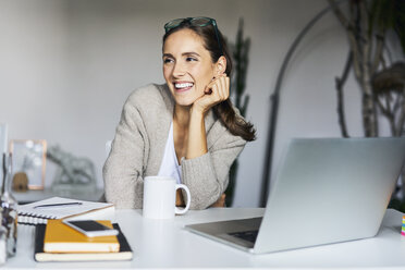 Happy young woman at home with laptop on desk - BSZF00171