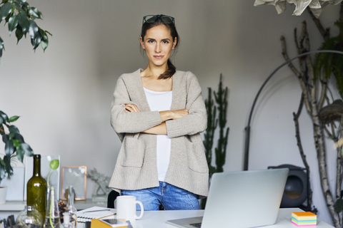 Confident young woman standing at desk with laptop stock photo