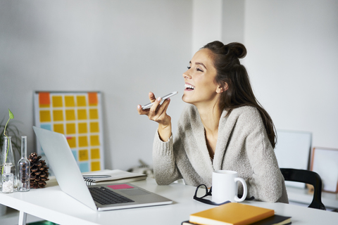 Happy young woman using smartphone at desk stock photo