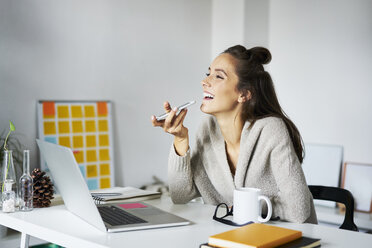 Happy young woman using smartphone at desk - BSZF00185