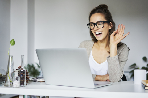 Young woman laughing during video chat at desk stock photo