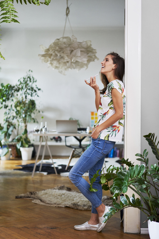 Happy young woman using smartphone at home stock photo