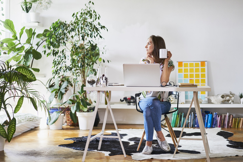 Junge Frau zu Hause am Schreibtisch mit Blick zur Seite, lizenzfreies Stockfoto