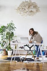 Smiling young woman at home using laptop on desk - BSZF00195