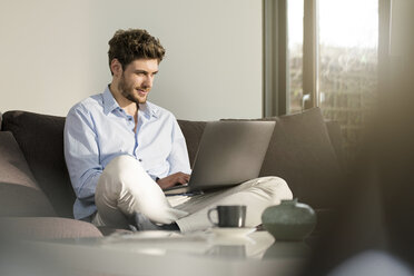 Mann sitzt zu Hause auf der Couch und benutzt einen Laptop - SBOF01257