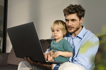 Vater und Sohn schauen zu Hause auf der Couch auf ihren Laptop - SBOF01258