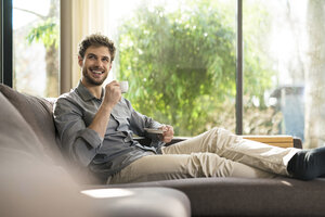 Lachender Mann, der sich zu Hause auf der Couch entspannt und Kaffee trinkt - SBOF01259
