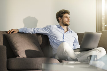 Man sitting on couch at home with laptop - SBOF01260