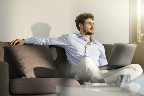 Mann sitzt auf der Couch zu Hause mit Laptop - SBOF01260