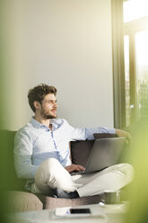 Man sitting on couch at home with laptop - SBOF01261