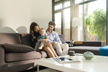 Smiling parents and son sitting on sofa at home - SBOF01265