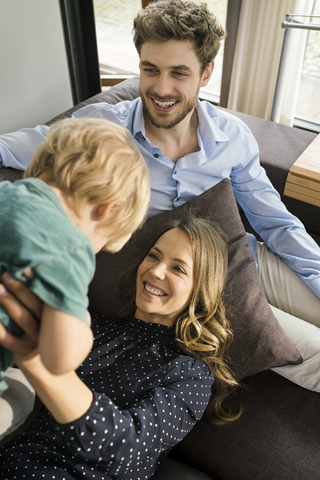 Glückliche Eltern spielen mit ihrem Sohn auf dem Sofa zu Hause, lizenzfreies Stockfoto