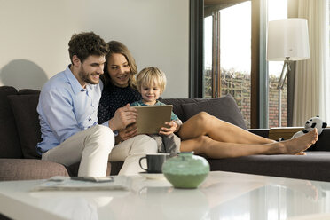 Eltern und Sohn sitzen zu Hause auf dem Sofa und halten ein Tablet in der Hand - SBOF01270