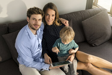 Portrait of smiling parents and son sitting on sofa with tablet at home - SBOF01272