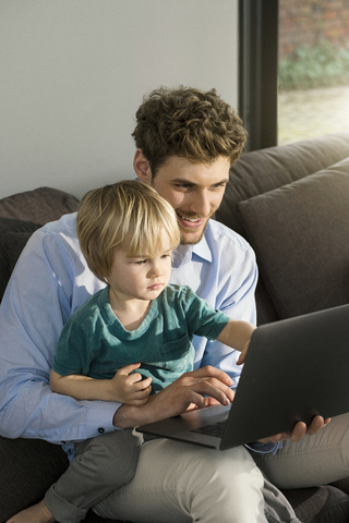 Vater und Sohn schauen zu Hause auf der Couch auf ihren Laptop, lizenzfreies Stockfoto