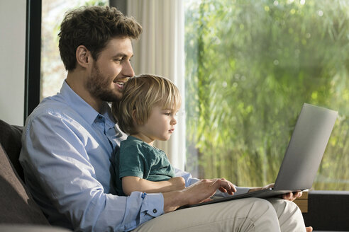 Vater und Sohn schauen zu Hause auf der Couch auf ihren Laptop - SBOF01277