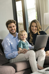 Portrait of happy parents and son sitting on sofa with laptop at home - SBOF01279