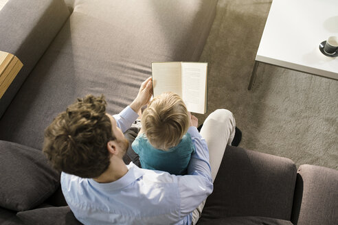 Vater und Sohn lesen ein Buch auf der Couch zu Hause - SBOF01283
