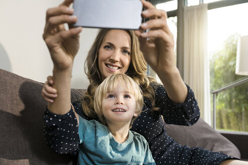 Lächelnde Mutter mit Sohn nimmt ein Selfie auf dem Sofa zu Hause - SBOF01285