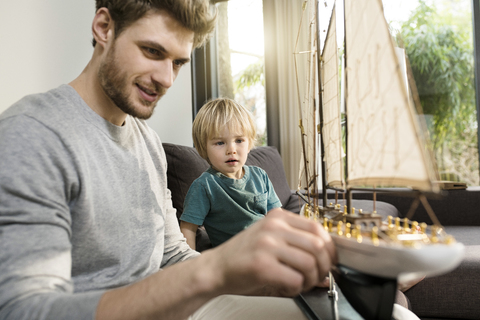 Vater und Sohn betrachten ein Spielzeugmodellschiff auf der Couch zu Hause, lizenzfreies Stockfoto