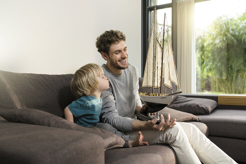 Vater und Sohn mit Spielzeugmodellschiff auf der Couch zu Hause - SBOF01288