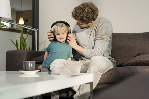 Vater setzt seinem Sohn auf der Couch zu Hause Kopfhörer auf - SBOF01290