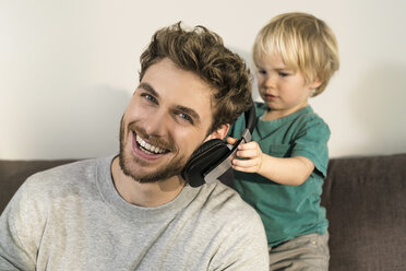 Happy father and son with headphones on couch at home - SBOF01291