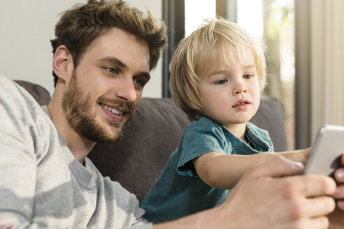Vater und Sohn schauen zu Hause auf der Couch auf ihr Smartphone - SBOF01292