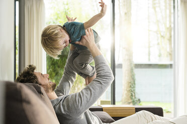 Happy father playing with son on sofa at home - SBOF01294