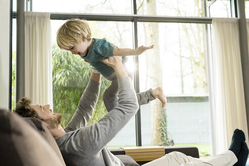 Happy father playing with son on sofa at home - SBOF01295