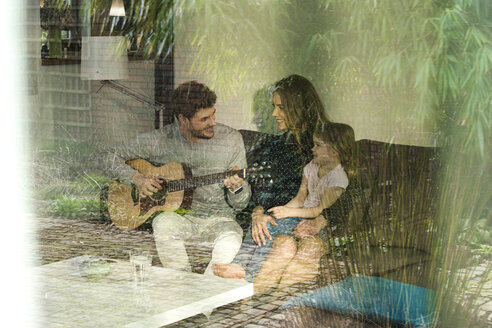 Glückliche Eltern und Tochter spielen Gitarre auf dem Sofa zu Hause - SBOF01302