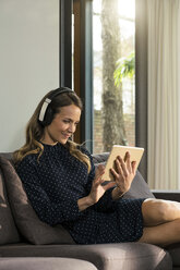 Smiling woman with tablet and headphones relaxing on couch at home - SBOF01306