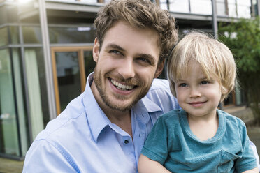 Portrait of smiling father with son in front of their home - SBOF01310
