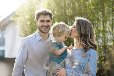 Happy family in garden in front of bamboo plants with mother kissing son - SBOF01320