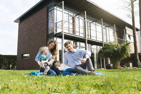 Porträt einer lächelnden Familie auf einer Decke im Garten vor ihrem Haus - SBOF01324