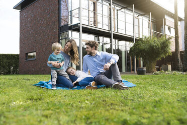 Glückliche Familie auf einer Decke im Garten vor ihrem Haus - SBOF01325