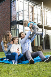 Happy family on blanket in garden in front of their home with father litfting up son - SBOF01326