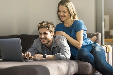 Lächelndes Paar benutzt Laptop auf Sofa zu Hause, lizenzfreies Stockfoto
