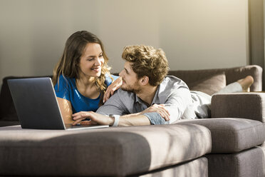 Smiling couple with laptop lying on sofa at home - SBOF01332