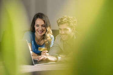 Smiling couple shopping online with laptop on sofa at home - SBOF01333