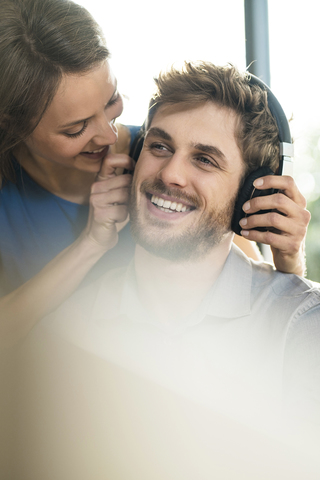 Lächelnde Frau, die ihrem Freund Kopfhörer aufsetzt, lizenzfreies Stockfoto