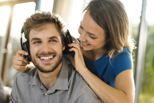 Lächelnde Frau, die ihrem Freund Kopfhörer aufsetzt - SBOF01342