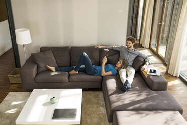 Couple with tablet and smartphone relaxing on sofa in modern living room at home - SBOF01344