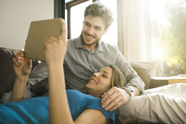 Lächelndes Paar schaut auf ein Tablet und entspannt sich auf dem Sofa zu Hause - SBOF01345