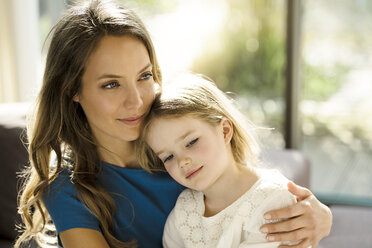Portrait of smiling mother holding her daughter in front of window - SBOF01350