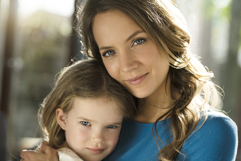 Porträt einer lächelnden Mutter mit Tochter vor einem Fenster, lizenzfreies Stockfoto