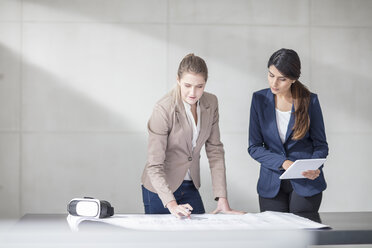 Zwei junge Frauen mit Tablet und VR-Brille arbeiten an einem Bauplan im Büro - ZEF14908