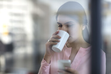 Porträt einer jungen Frau mit Mobiltelefon und Kaffee im Büro - ZEF14930