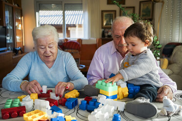 Urgroßeltern und kleines Mädchen spielen zusammen mit Plastikbausteinen zu Hause - GEMF01857